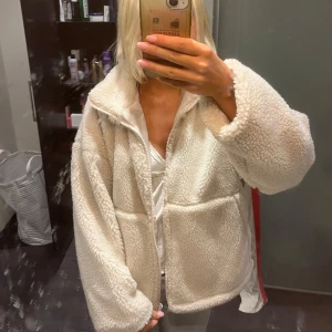 Beige teddyjacka med dragkedja - Mysig och oversized teddyjacka i beige med fluffig yta och stora fickor framtill. Jackan har lång ärm och stängs med dragkedja. Perfekt för att hålla sig varm och se chill ut under höst och vinter. Passar dig som gillar en avslappnad och trendig stil.