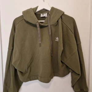 Olivgrön croppad hoodie från Adidas - Perfekt för chill dagar och har en loose passform som ger en avslappnad vibe.