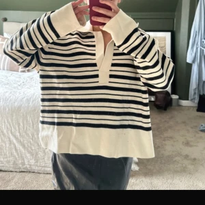 Randig stickad tröja från Second Female - Säljer en oversized stickad tröja från Second Female i storlek L. Tröjan är vit med svarta ränder, har v-ringad hals och långa ärmar. Materialet är 100% bomull vilket gör den mjuk och skön samt nopprar inte. Perfekt för chill dagar och snygg till jeans