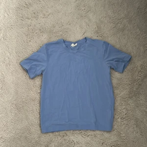 Ljusblå t-shirt från Gina Tricot - En enkel och fräsch ljusblå t-shirt från Gina Tricot, kollektionen basicallybasics. Modellen är klassisk med rund hals och korta ärmar. Perfekt för dig som gillar cleana och stilrena plagg. Materialet är mjuk bomull som känns skönt mot huden.