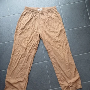 Bruna linnebyxor från Pier One - Snygga bruna linnebyxor från Pier One med avslappnad passform och elastisk midja. Byxorna har raka ben, sidofickor och bakfickor med knapp. Perfekta för chill dagar och sommarhäng. Lätta och luftiga i materialet.