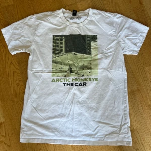 Arctic Monkeys The Car t-shirt vit - Vit t-shirt med tryck från Arctic Monkeys album 'The Car' på bröstet. Officiell bandmerch, beställd från deras egen merch-shop. Klassisk rund hals och korta ärmar. Tjock, kvalitativ bomull. 