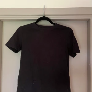 Svart t-shirt från Lyle & Scott Junior - En enkel svart t-shirt från Lyle & Scott Junior med rund hals och korta ärmar. T-shirten är gjord i mjuk bomull och har en klassisk passform som funkar till det mesta. Perfekt för dig som gillar stilrena och basic plagg.