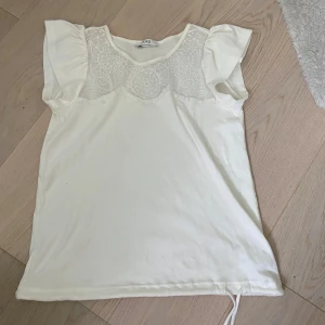 Vit blus med spets från Jorli - Supersöt vit blus från Jorli med spetsdetaljer över bröstet och axlarna. Blusen har korta, voluminösa ärmar och ett mjukt tyg i bomull. Spetsen har ett broderat mönster som ger en extra touch. Perfekt för dig som gillar romantisk och clean stil.