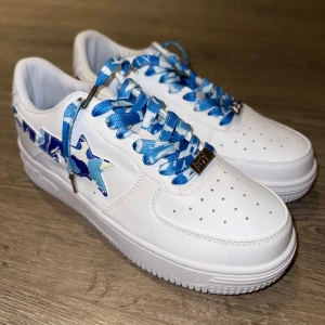 BAPE STA sneakers med blå camo - Säljer ett par vita BAPE STA sneakers i vitt läder med ljusblå camo på sidan och matchande skosnören. Storlek 45 helt nya