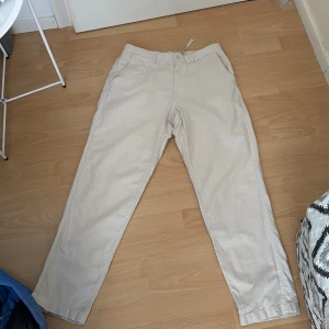 Beige linnebyxor  från Uniqlo, storlek M - Snygga beige linnebyxor från Uniqlo i storlek M, midja 76-84 cm. Byxorna har klassisk rak passform, bälteshällor och sidfickor. Tillverkade i mjuk bomull med lite stretch för extra komfort. Perfekta för en clean och chill look.