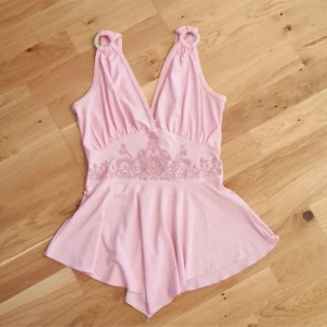 Rosa topp med pärlbroderi - Supersöt ljusrosa topp med v-ringad omlott upptill och bred volang nedtill. Toppen har axelband med ringdetaljer och ett vackert pärlbroderi med små paljetter över midjan. Köpt i början på 2000-talet, men inte använts. Har någon gulaktig fläck som jag inte testat att ta bort med fläckbortagning