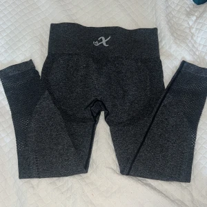 Mörkgrå seamless träningsbyxor från X - Snygga mörkgrå seamless träningsbyxor från X med hög midja och diskret logga framtill. Materialet är stretchigt och andas, perfekt för gymmet. De har mesh-detaljer längs benen för extra ventilation och en tight passform som framhäver formen!😊