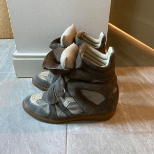 Isabel Marant skor - Säljer ett par höga sneakers från Isabel Marant i grått och beige med coola paneler och kardborreband. Skorna har en platt gummisula, rund tå och är tillverkade i mocka och skinn. Defekter finns men som syns på bilderna