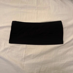 Svart bandeau tubtopp - En stilren svart bandeau tubtopp som är perfekt för att skapa en clean och enkel look. Toppen är axelbandslös och har en tight passform som sitter snyggt mot kroppen. Materialet känns mjukt och stretchigt, vilket gör den bekväm att bära hela dagen.