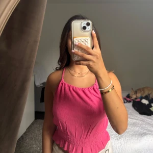 Rosa linnetopp med smock och korsade band - Säljer en superfin rosa linnetopp med smockad nederkant och tunna axelband som korsas i ryggen. Toppen har en lätt rynkad struktur och är croppad, vilket ger en chill vibe! Perfekt för varma dagar och snygg att styla med jeans eller kjol!💞