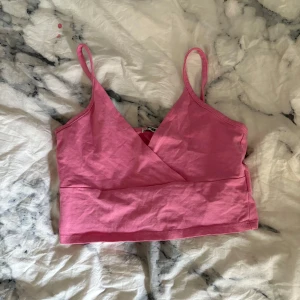 Rosa omlott linnetopp från FB Sister - Supersöt rosa linnetopp från FB Sister i storlek XS. Toppen har smala axelband, omlott-skärning framtill och croppad passform. Perfekt för varma dagar och enkel att matcha med jeans eller kjol. Tillverkad i mjuk bomull för en skön känsla.