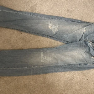 Ljusblå slitna jeans från Dondup - Säljer ett par ljusblå jeans från Dondup med slitningar och lagade detaljer på både fram- och baksida. Det är wide 32 och motsvarar storlek M