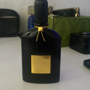 Tom Ford Black Orchid 50ml EdP - Tom Ford Black Orchid Eau de Parfum i en lyxig svart flaska med räfflad yta och gulddetaljer. Flaskan rymmer 50 ml och har en elegant, exklusiv look med guldplakett och snöre runt halsen. Perfekt för dig som gillar unika och djupa dofter.