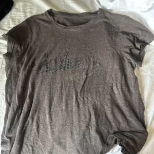 Brun Zadig  t-shirt med strass - Brun t-shirt från zadig voltaire med glittrande strassdetaljer som bildar loggan på bröstet. Klassisk rund halsringning och korta ärmar. Perfekt för dig som gillar en chill men ändå snygg vibe.