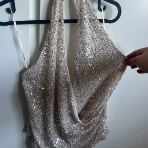Silver paljettopp från Gina Tricot XL - Snygg draperad topp i silver från Gina Tricot, täckt med glittrande paljetter. Modellen är ärmlös med tunna axelband och har en djup urringning framtill. Perfekt för dig som vill sticka ut med en riktigt glittrig vibe. Aldrig använd. 