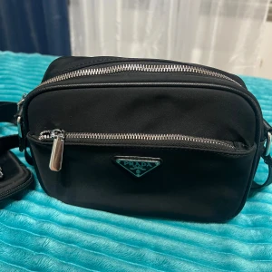 Prada axelväska  - En helt ny Prada axelväska som finns till salu. Får du inte plats med alla din saker i dina fickor eller är rädd att något?, då så har vi en lösning att ha en axelväska. 