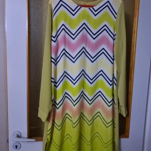 Mönstrad långärmad klänning i pastell - Fin långärmad klänning med pastellgult tyg och framsida i vitt med färgglada zickzack-ränder i rosa, lime och svart. Mjukt, lätt material och dragkedja bak. Manschett med knappdetalj på ärmen. Den är köpt i Turkiet, och Sparsamt använd :)