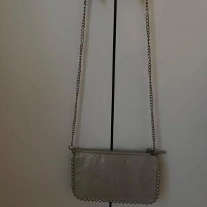 Liten handväska Zara  - Snygg beige axelväska i mocka med silverfärgade nitar längs kanterna och en cool kedjerem. Väskan har dragkedja upptill och flera fack inuti, perfekt för att hålla ordning på dina grejer. Stilren och trendig design. Från Zara och utan några defekter. Säljer eftersom den inte används💓