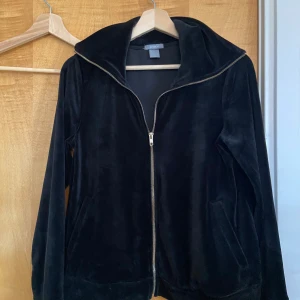 Svart velourjacka från Lindex M - Mjuk svart jacka i velour från Lindex med hel dragkedja framtill och hög krage. Jackan har långa ärmar och två fickor på sidorna. Perfekt för dig som gillar en chill och stilren look. Har aldrig använt den då den bara blivit bortglömd i garderoben.