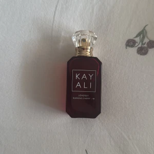Kayali Lovefest Burning Cherry parfym - Kayali Lovefest Burning Cherry är en lyxig parfym i en mörkröd, fyrkantig glasflaska med gulddetaljer och en kristalliknande transparent kork. Doften har en söt och fruktig cherry vibe, perfekt för dig som gillar unika och trendiga parfymer.