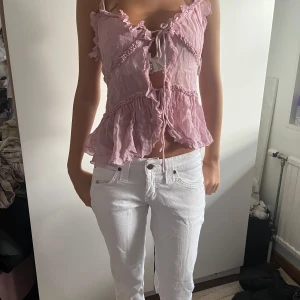 Ljusrosa volangig blus med knyt - Supersöt ljusrosa blus med volanger och knyt framtill. Tunt, luftigt tyg och ärmlös modell med romantiska detaljer och lätt rynkade sömmar. Perfekt för varma dagar och en feminin look.