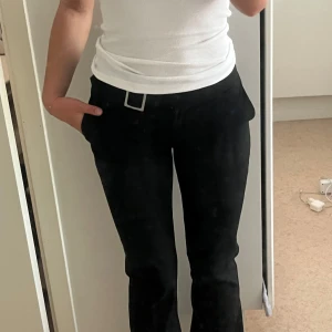 Svarta kostymbyxor med bälte - Snygga svarta kostymbyxor med låg midja och raka ben. Byxorna har en stilren silverspänne-detalj i midjan och sidfickor. 