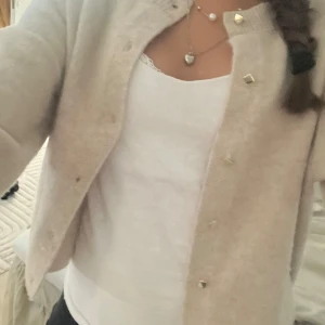 Beige kofta med guldknappar - Supermjuk och stilren beige kofta med snygga guldiga knappar framtill. Koftan har en rak passform och är långärmad, perfekt att slänga på sig över en topp. Materialet känns fluffigt och mysigt, passar perfekt för lager-på-lager.