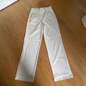 Beiga utsvängda kostymbyxor - Snygga beiga kostymbyxor med utsvängda ben och hög midja. Byxorna har klassiska fickor fram och hällor för bälte. Perfekta för en clean och stilren look. Materialet känns mjukt och har en lätt stretch för extra komfort. Finns en liten fläck på ena benet. Inte säker på verken storlek eller märke, men de passar som 36