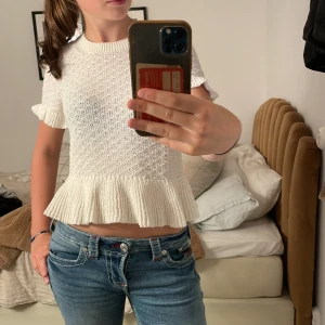 Vit stickad topp med volangkant - Använd EN gång‼️. Supersöt vit stickad topp med korta ärmar och volangkant nertill. Toppen är croppad och har en rund halsringning samt ribbade detaljer vid ärmslut och nederkant. Perfekt för dig som gillar en feminin och trendig stil.