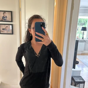 Svart v-ringad topp Comptoir des Cotonniers - Säljer en svart långärmad topp från Comptoir des Cotonniers med unik v-ringning och snygg omlott-detalj framtill. Materialet känns mjukt och bekvämt, perfekt för dig som gillar stilrena plagg med en twist. Ingen polyester.