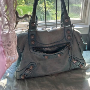 Blå Balenciaga City handväska i skinn - Cool Balenciaga City handväska i ljusblått skinn med silvriga nitar och dragkedja framtill. Väskan har flätade handtag och klassiska detaljer som ger en edgy vibe. Perfekt storlek för allt du behöver och en ikonisk look som sticker ut.