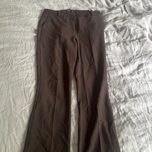 Bruna vilma kostymbyxor - Snygga bruna kostymbyxor med bootcut-snitt och klassiska pressveck. Byxorna har hällor för bälte och sidfickor, perfekta för en stilren och trendig look. Passar dig som gillar en tidlös och clean stil.