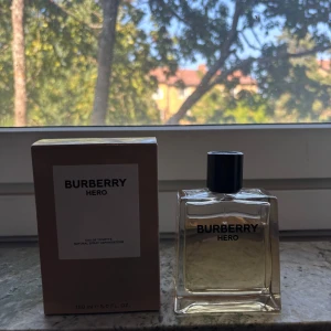 Burberry Hero Eau de Toilette 150ml - Burberry Hero Eau de Toilette i en stilren, fyrkantig glasflaska med svart lock och klassisk logga. Doften kommer i en beige kartong med minimalistisk design. Flaskan rymmer 150 ml och finns ca 120 ml kvar. Denhar en ljusgul vätska. Perfekt för dig som gillar exklusiva och moderna parfymer.