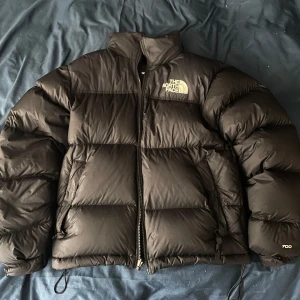 Svart pufferjacka från The North Face - Säljer en svart pufferjacka från The North Face i storlek XS. Jackan har hög krage, dragkedja framtill och två sidofickor. Klassisk 700-fill dunjacka med logga på bröstet och ärmen. Perfekt för kalla dagar och riktigt snygg streetstil.