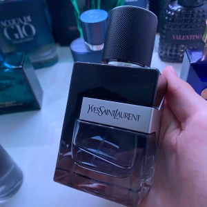  BYTE - Snygg parfymflaska från Yves Saint Laurent med svart och transparent glas, silverdetalj och stor svart kork med textur. Flaskan har en modern, stilren design och känns lyxig att hålla i handen.