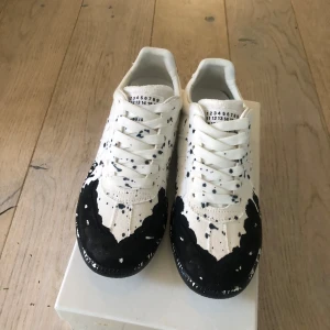 Maison Margiela paint splatter  - Maison Margiela sneakers i vitt med svart färgstänk och coolt splattermönster. Klassisk rund tå, snörning och platt sula. Ovandel i skinn och textil. Märkets ikoniska etikett på plösen och sula med präglad logga. Kommer med originalkartong och dustbags. Galet feta inför sommaren och passar till allt, riktigt unika och lyfter hela din outfit, priset är inte fast så kom med bud💯✅