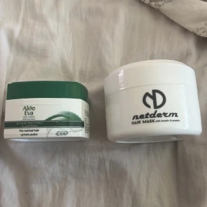 Aloe Eva hårkräm & Netderm hårmask - Två hårprodukter: Aloe Eva hårkräm med aloe vera-extrakt i grönvit burk, perfekt för normalt hår. Netderm hårmask i vit burk med keratin och protein, passar alla hårtyper och innehåller bland annat olivolja och grönt te-extrakt. Båda är återfuktande och vårdande.