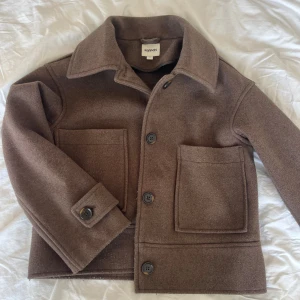 Brun overshirt i ull från Kappahl XS - Säljer en brun overshirt från Kappahl i storlek XS. Jackan är i ullmaterial, har stora fickor framtill, klassisk krage och knäppning med knappar. Perfekt för lager-på-lager och en chill look under höst och vinter.