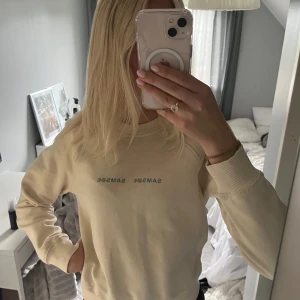 Beige sweatshirt från Samsøe Samsøe - Säljer en beige sweatshirt från Samsøe Samsøe med diskret logga framtill. Tröjan har rund halsringning, långa ärmar och ribbade muddar vid ärmslut och nederkant. Perfekt för en chill och stilren look.