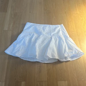 Vit volangkjol från H&M, stl 38 - Superfin vit kortkjol från H&M i storlek 38. Kjolen har broderade blommor och volangig nederdel.
