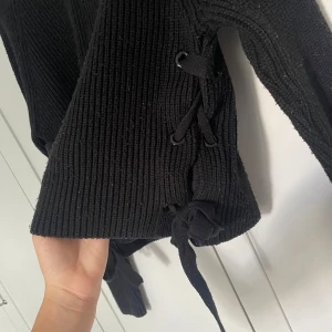 Svart stickad tröja med knytningar - Svart stickad tröja från Stradivarius i storlek M. Tröjan har långa ärmar och cool snörningsdetalj i sidorna som ger en unik look. Perfekt för lager-på-lager och passar till både jeans och kjol.