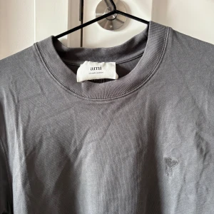 Grå t-shirt från Ami Paris - Herr Snygg grå t-shirt från Ami Paris med diskret broderad logga på bröstet. Klassisk rund halsringning och korta ärmar. Köpt på NK Göteborg för 2081 kr använd fåtal gånger då de var fel storlek.