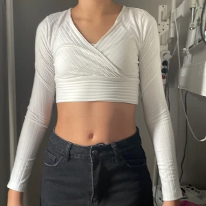 Vit omlott croppad topp från SHEIN - Säljer en vit croppad topp från SHEIN i omlottmodell med v-ringning. Toppen har långa ärmar och är ribbad för en snygg struktur. Perfekt för dig som gillar stilrena och trendiga plagg med lite edge.