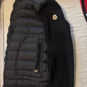 Moncler Cardigan - Säljer en svart cardigan från Moncler. Jackan har dragkedja framtill och på fickorna samt Moncler-logga på ena ärmen. Perfekt för våren den är knappt använd och i perfekt skick. Storlek L men passar till M OBS!! Tar inga byten
