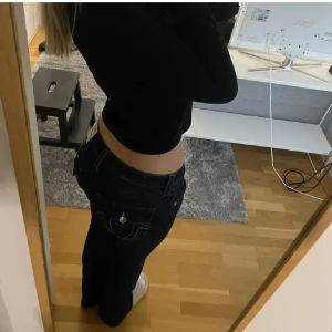 True Religion Becca Bootcut Jeans - Säljer ett par mörkblå True Religion Becca jeans med bootcut och midwaist. Jeansen har snygga kontrastsömmar, ikoniska ficklock med silverfärgade knappar och klassisk True Religion patch bak. Perfekt för dig som gillar en tidlös och cool look.