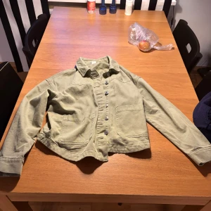 Grön jeansjacka  från Vero Moda - Snygg grön jeansjacka från Vero Moda i manchestertyg. Jackan har klassisk krage, stora fickor framtill och knäppning med silvriga knappar. Perfekt att slänga över en hoodie eller t-shirt för en chill look.