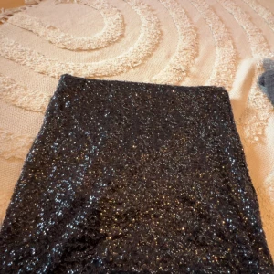 Svart glittrig paljettkjol - Säljer en svart kortkjol täckt av glittriga paljetter. Kjolen har en tight passform men är väldigt stretchig