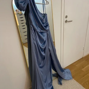 Blå långklänning med drapering - Elegant blå långklänning med draperad design och one shoulder. Perfekt för speciella tillfällen som tex bal eller bröllop med sin flytande siluett och mjuka material. Har använt den en gång 