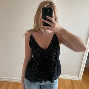 Svart glittrig linnetopp från Zara - Supersnygg svart linnetopp från Zara med tunna axelband och v-ringning. Toppen har glittriga detaljer i form av små silverfärgade pärlor som bildar mönster över hela plagget. HELT NY ALDRIG ANVÄND!! Köptes för ca 500kr Den är i storlek L men passar bra på mig som i vanliga fall har xs😅🥰